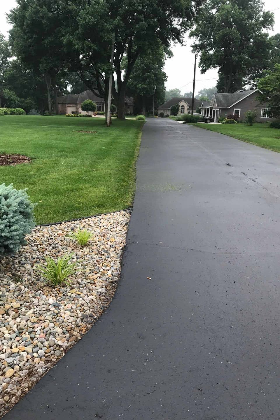 Long asphalt driveway with green lawns and trees on both sides.