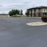 Empty parking lot next to a gray, two-story building under a cloudy sky.