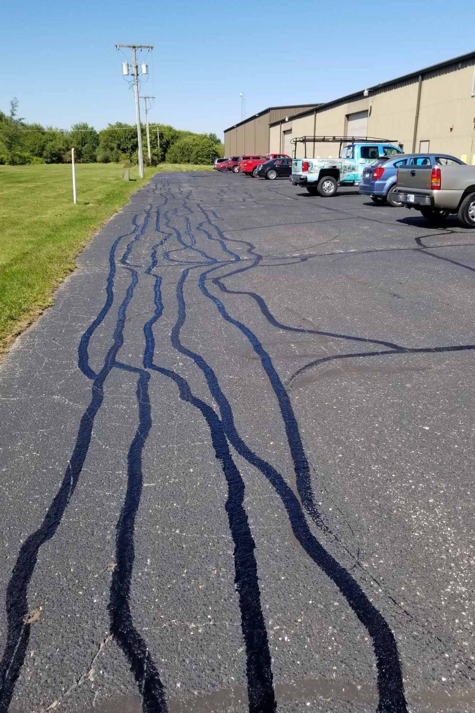 Asphalt maintenance evident in fresh tar cracks; cars lined on the right.