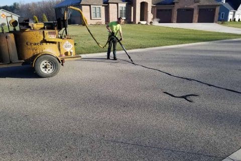 Worker sealing cracks on asphalt road with a machine.