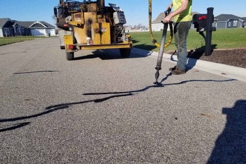 Worker using machinery for asphalt maintenance on a residential street.