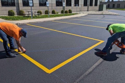 Two workers painting yellow lines in an empty lot for commercial asphalt services.