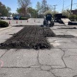 Small vehicle conducting asphalt repair in a parking lot.