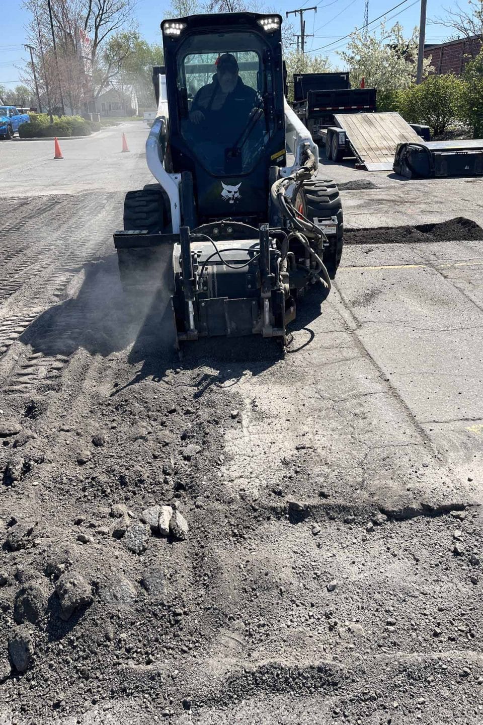 A skid steer loader handling asphalt repair on a construction site.