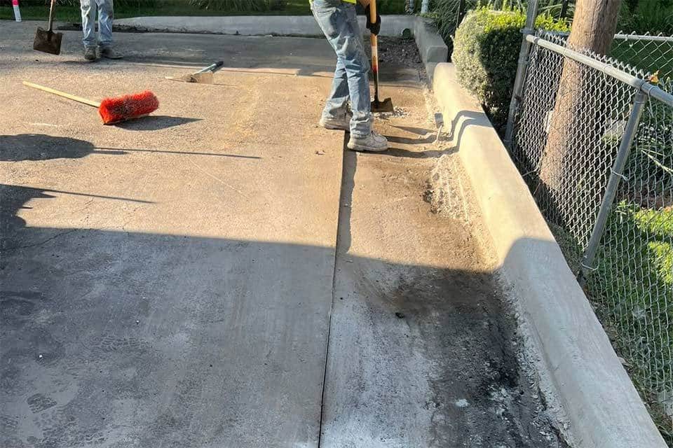 Workers repairing a concrete sidewalk near an asphalt repair site.