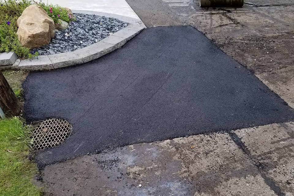 Asphalt repair patch beside a drainage grate, freshly laid.