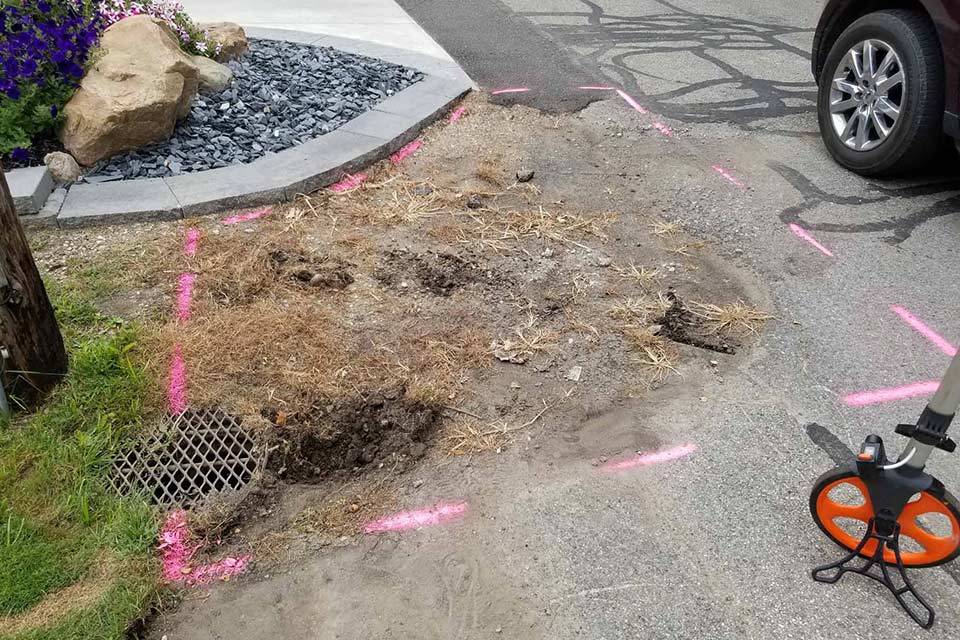 Dug-up roadside area for asphalt repair, pink markings near parked car.