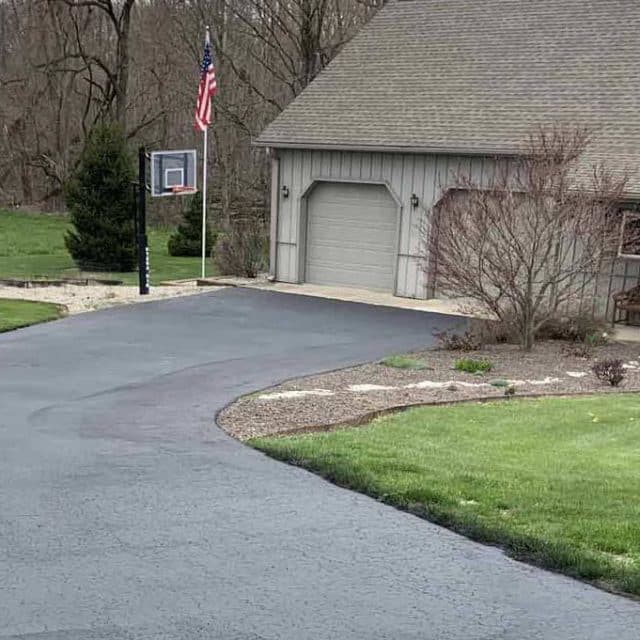 Asphalt driveway with an SUV, basketball hoop, and a house boasting a flag.