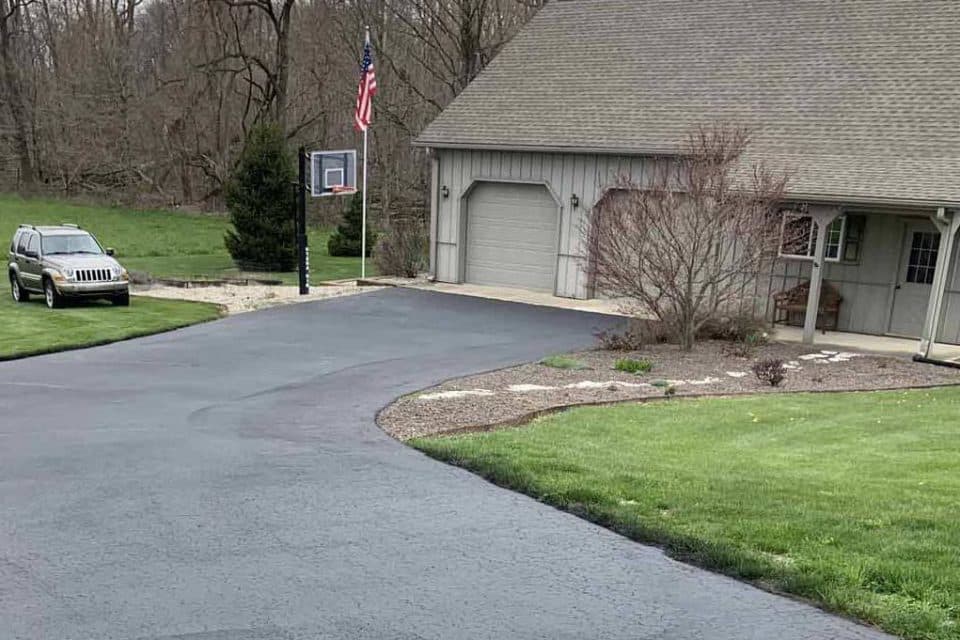 Asphalt driveway with an SUV, basketball hoop, and a house boasting a flag.