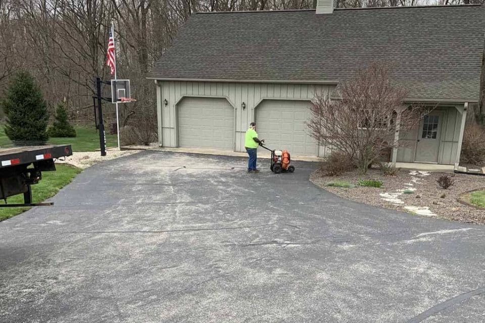 Person working on asphalt maintenance near a garage and basketball hoop.