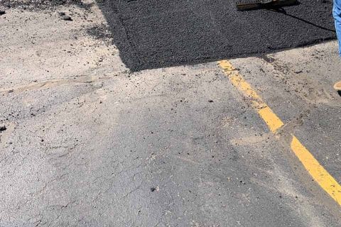 Workers spreading asphalt on a paved surface with shovels.