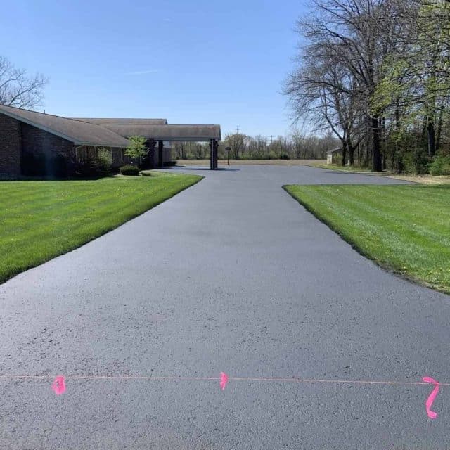 Freshly paved driveway leading to a house surrounded by trees and grass.