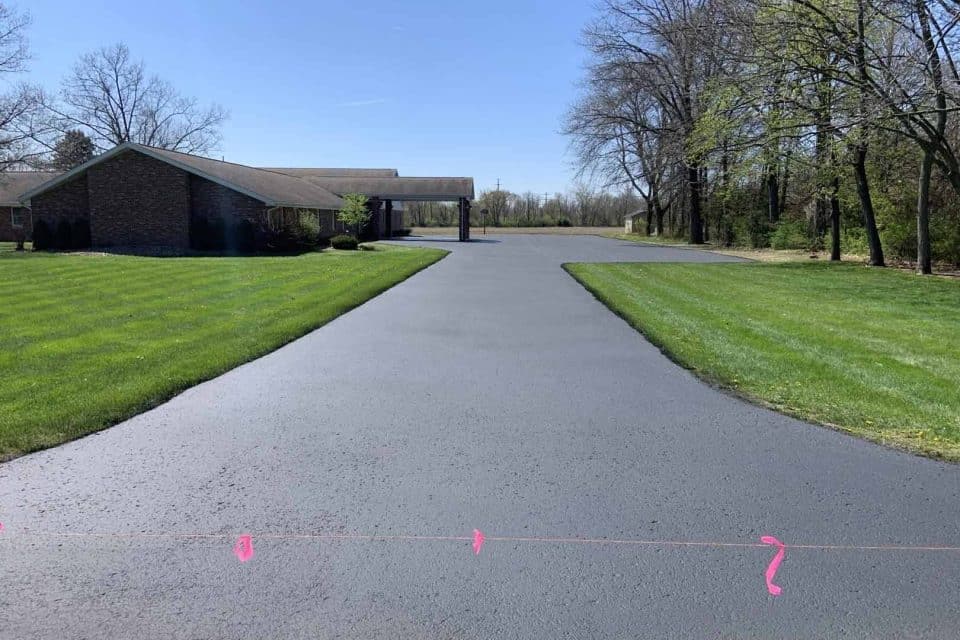 Freshly paved driveway leading to a house surrounded by trees and grass.