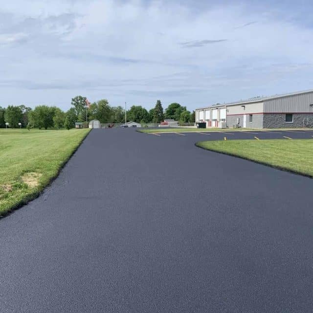 Freshly paved asphalt road leading to a building, flanked by grass.