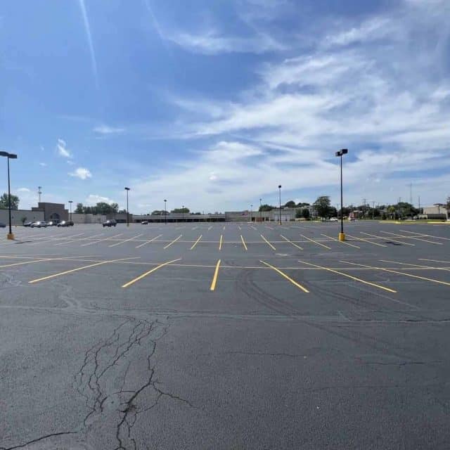 Sealcoated parking lot under a clear sky with scattered clouds.