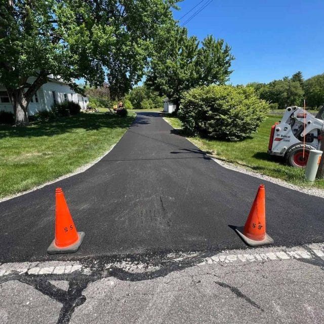 Freshly paved driveway with two orange cones at the entrance.