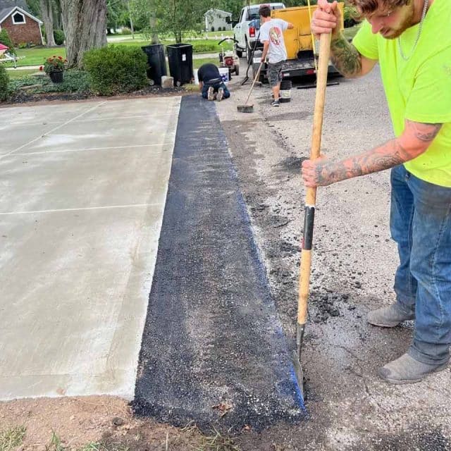 Workers laying asphalt next to a concrete driveway.