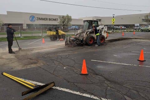 Roadwork in progress with machinery and cones at a parking lot.