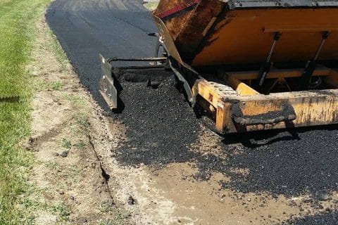 Commercial asphalt services paving new roads near trees and signs.