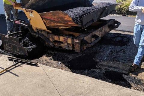 Workers perform asphalt paving on a residential road.