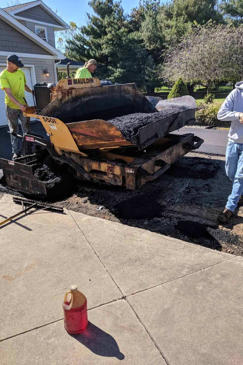 Workers perform asphalt paving on a residential road.