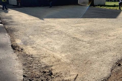 Wide driveway with gravel surface in front of a large black building.