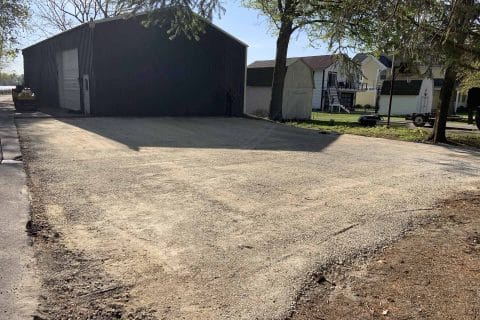 Gravel driveways span a lot in front of a large, dark building under clear skies.