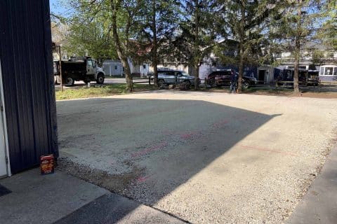 Gravel area marked with pink lines near trees and buildings.