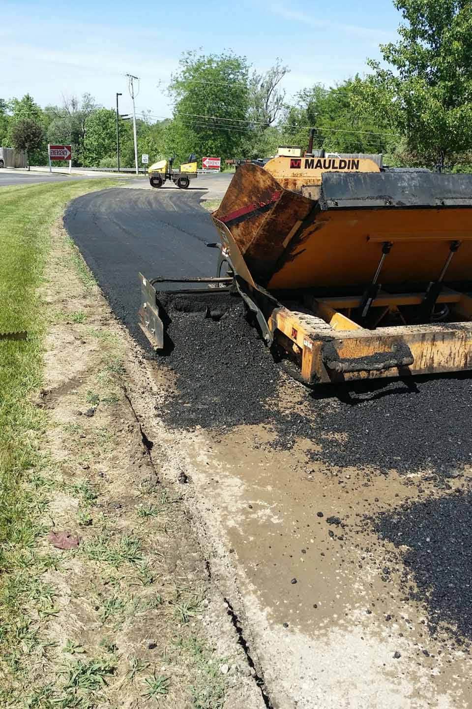 Commercial asphalt services paving new roads near trees and signs.