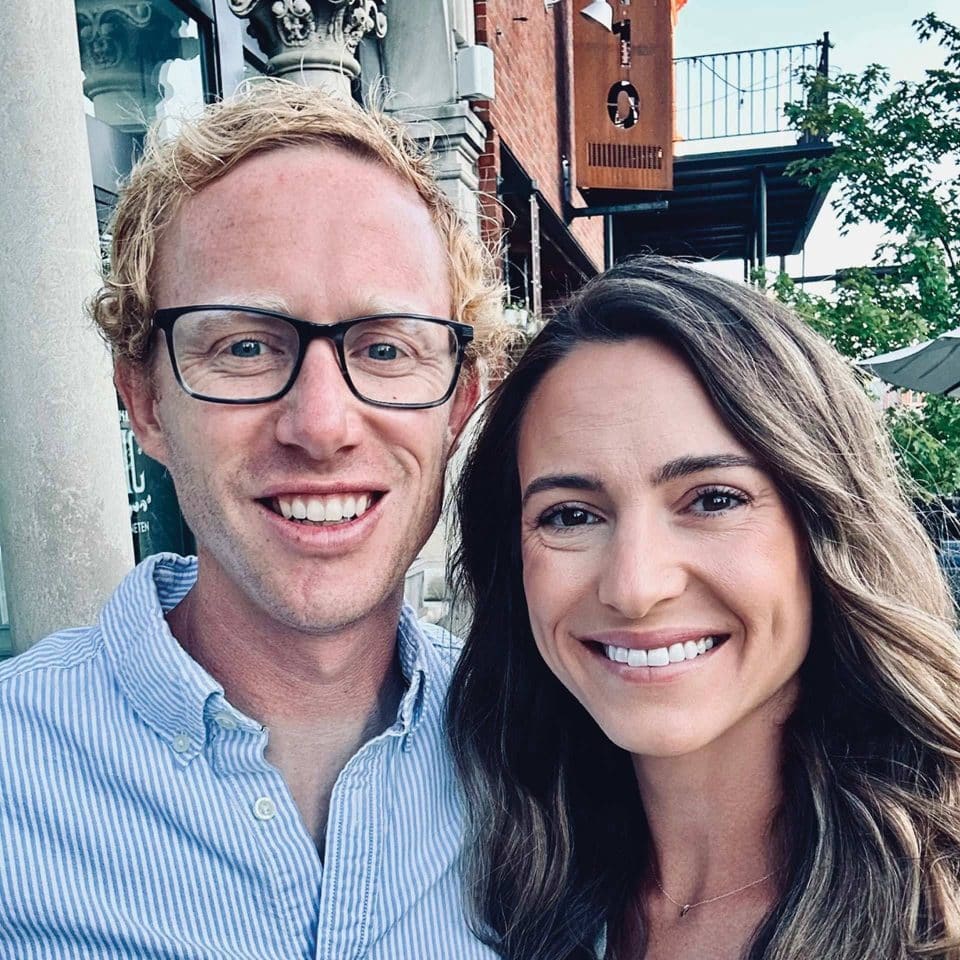 A man and woman smiling for a selfie outdoors.