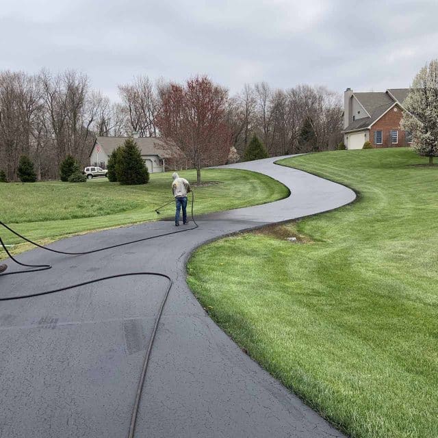 Two workers sealcoating a residential driveway in a suburban area.