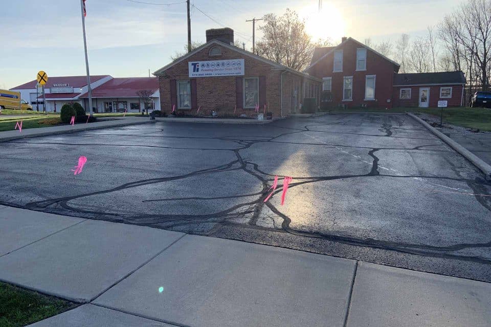 Vacant lot with asphalt maintenance cracks, pink markers by a brick building.