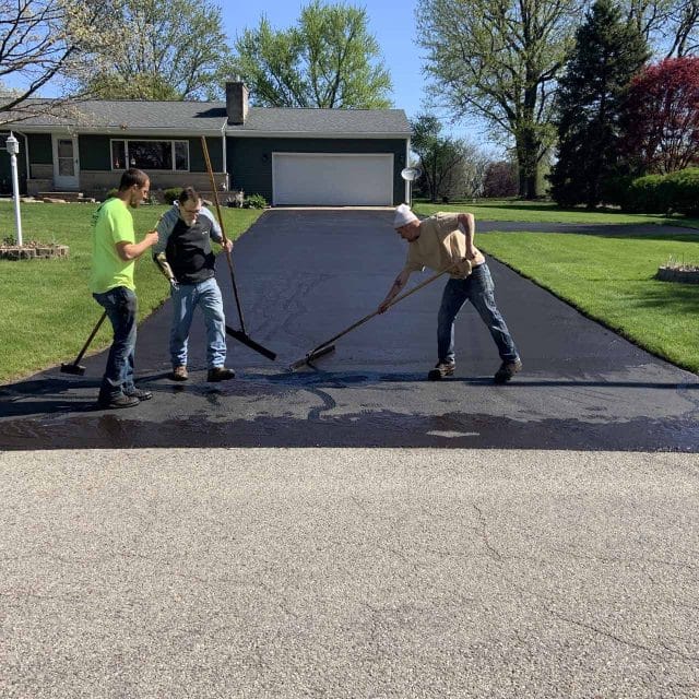 Three people are driveway paving on a residential lot.