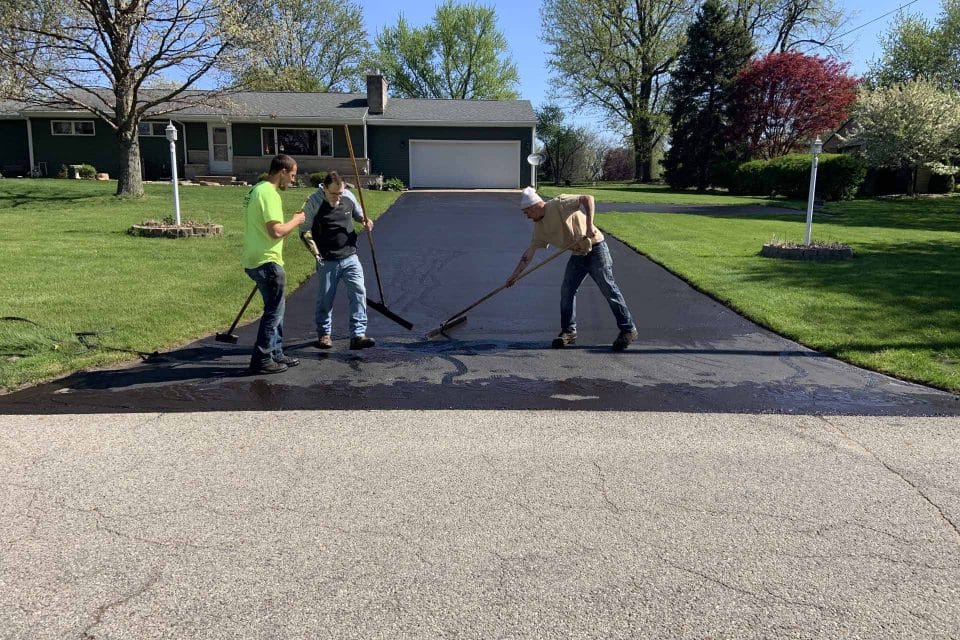 Three people are driveway paving on a residential lot.