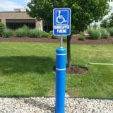 Handicapped parking sign on a blue pole near a building and trees.