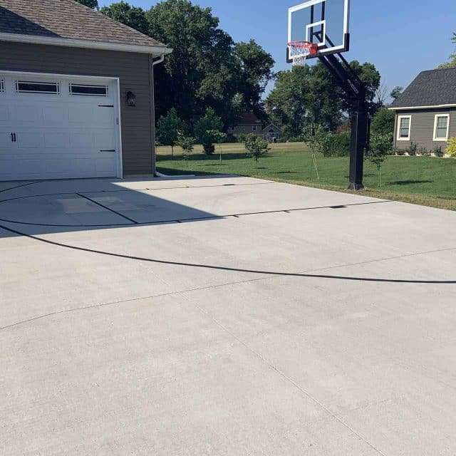 Asphalt driveway with basketball hoop and painted court lines.