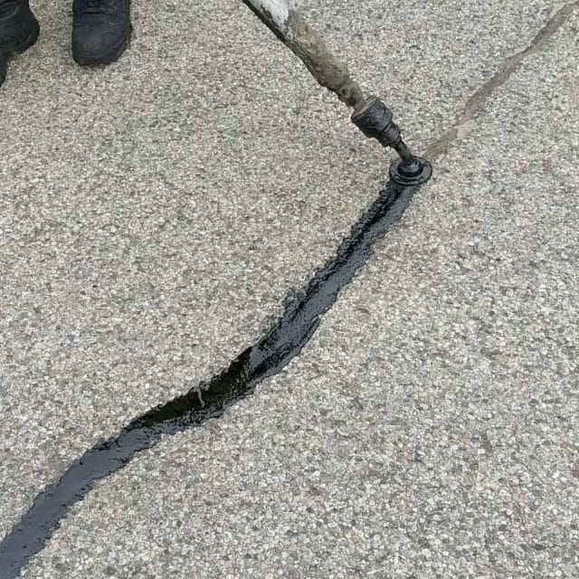 Applying black sealant to a crack in gray pavement.