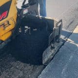 Road crew operating asphalt paving machine on a street.